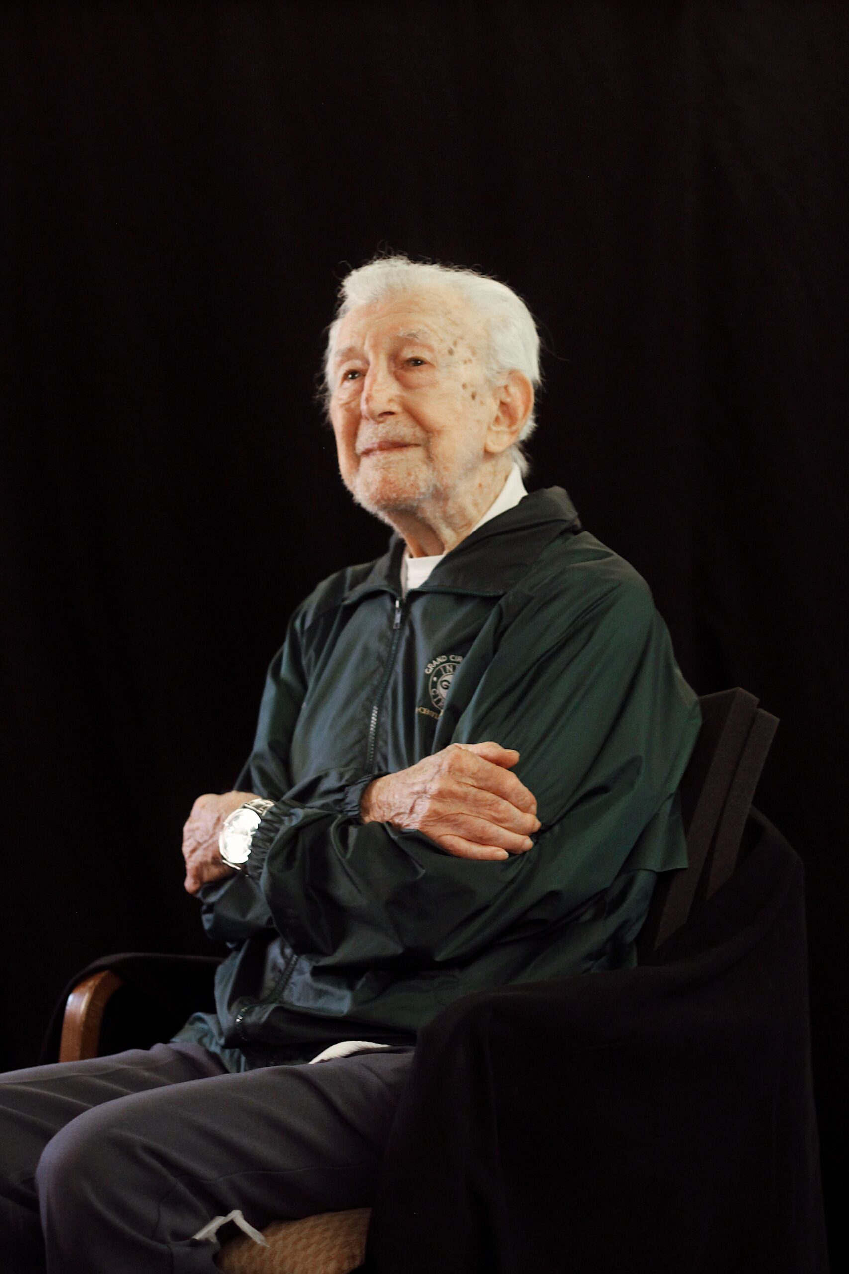 Elderly veteran wearing a dark jacket while seated on a stage.