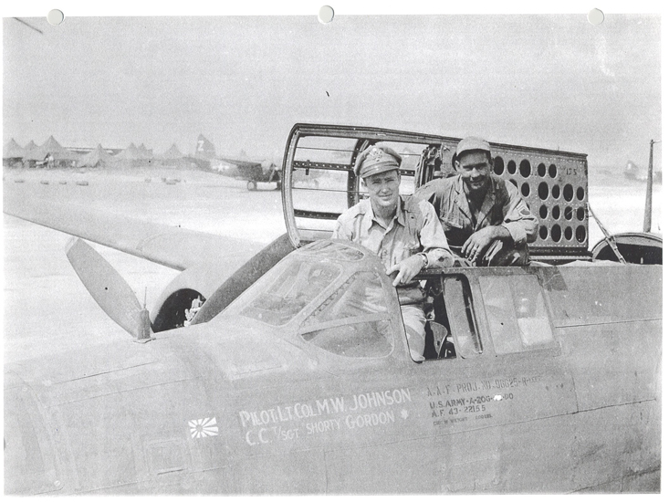 A black-and-white photograph depicting military personnel on an aircraft. The photo shows two men, one sitting in the cockpit while the other man is visible at the side of the cockpit, both wearing military uniforms and hats.