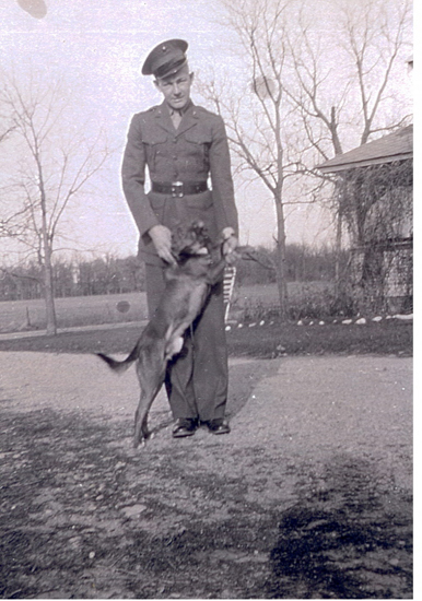 Serviceman standing outdoors in a military uniform with a dog.
