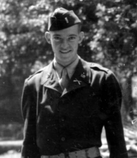 Smiling young serviceman standing outdoors in a military uniform.