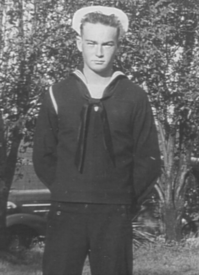 Sailor standing outdoors in a dark U.S. Navy uniform.