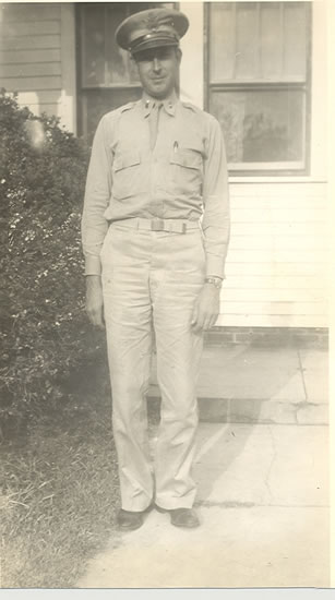 Serviceman standing outside a building in a light-colored military uniform.