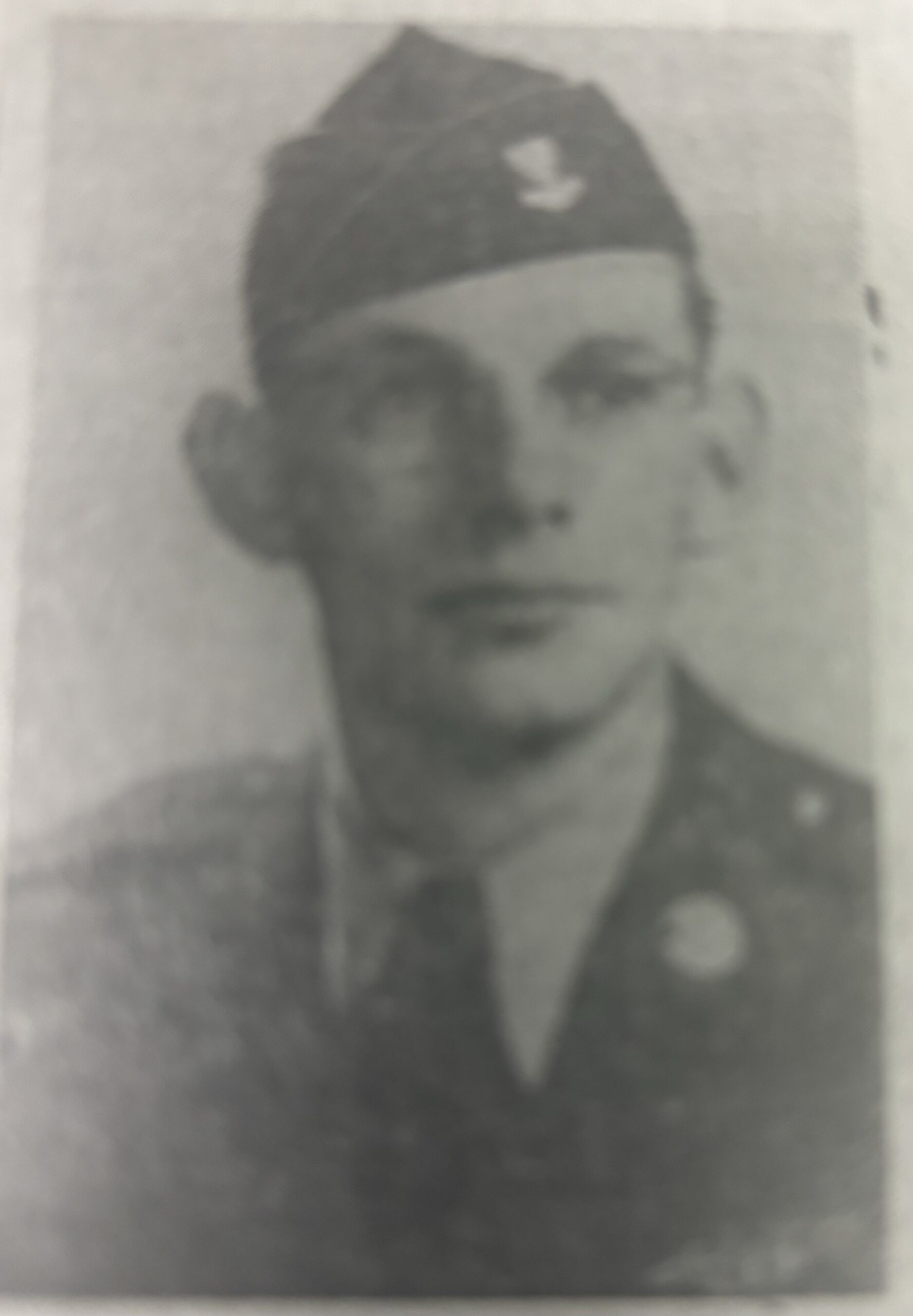 Serviceman wearing a military uniform and garrison cap in a faded portrait.