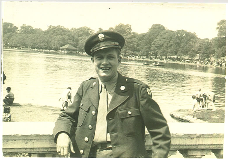 Smiling serviceman wearing a military uniform beside a body of water.