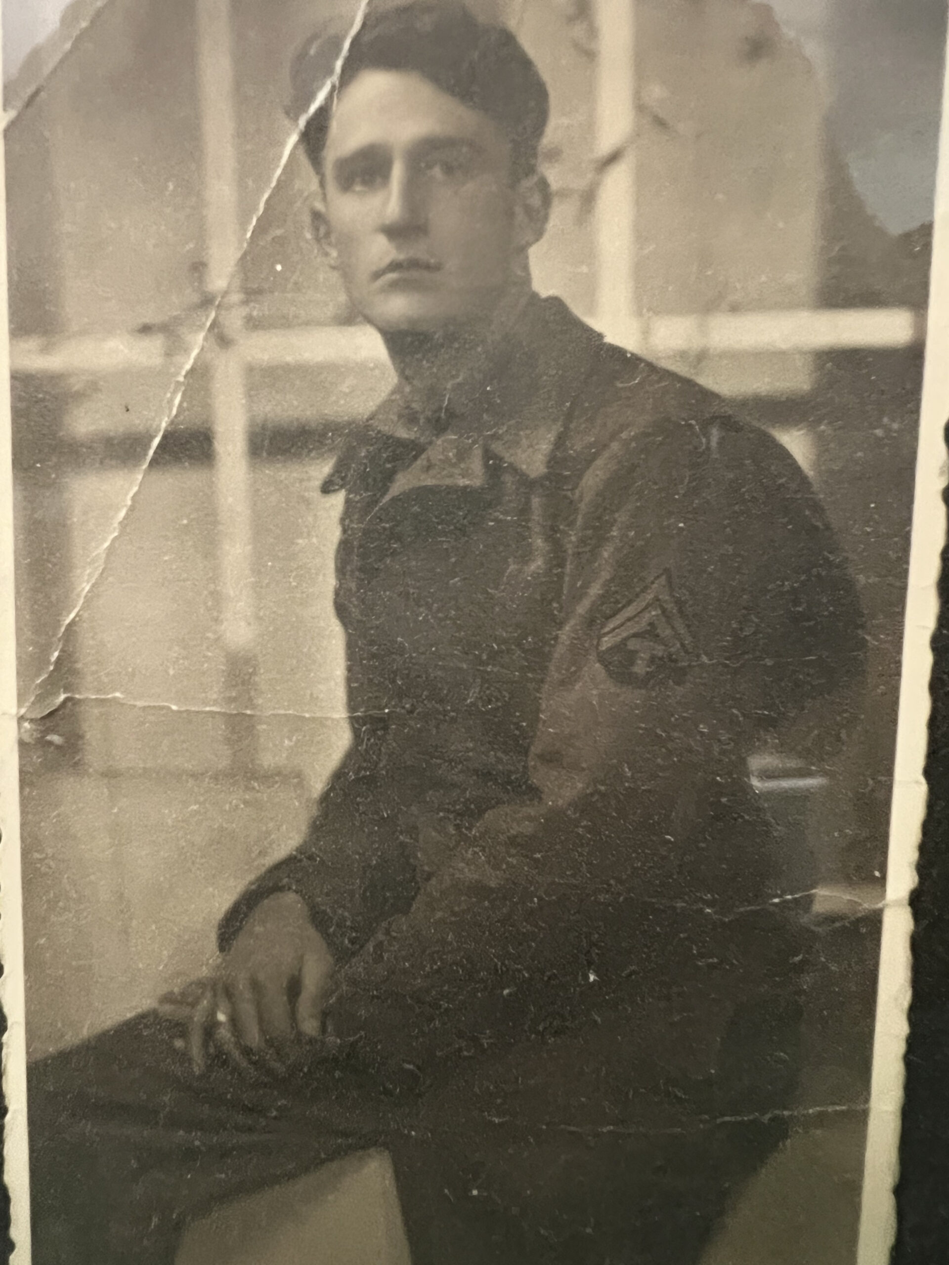 Serviceman seated indoors in a military uniform with sergeant’s stripes.