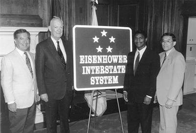 Dwight D. Eisenhower and another man display an Eisenhower Interstate System sign.