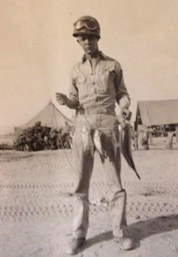 Serviceman standing outdoors while holding several large fish.