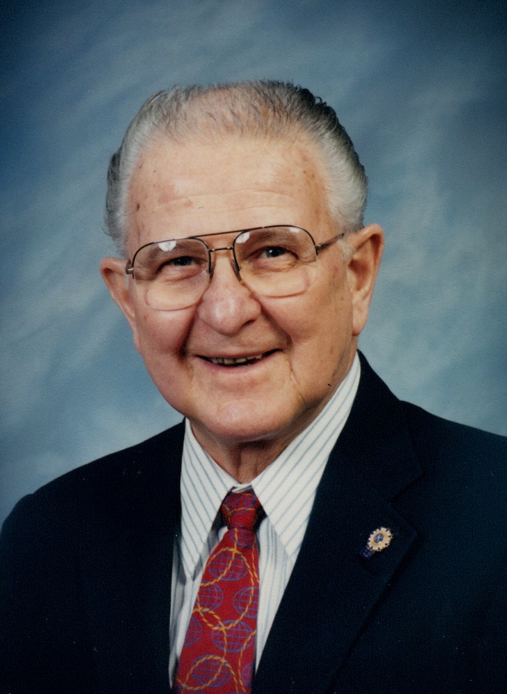 Older man wearing glasses, a suit, and a tie in a formal portrait.