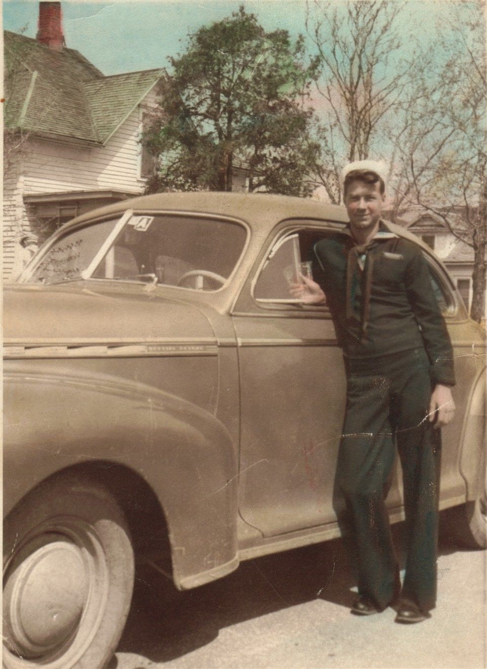 Serviceman standing beside a vintage car in a military uniform.
