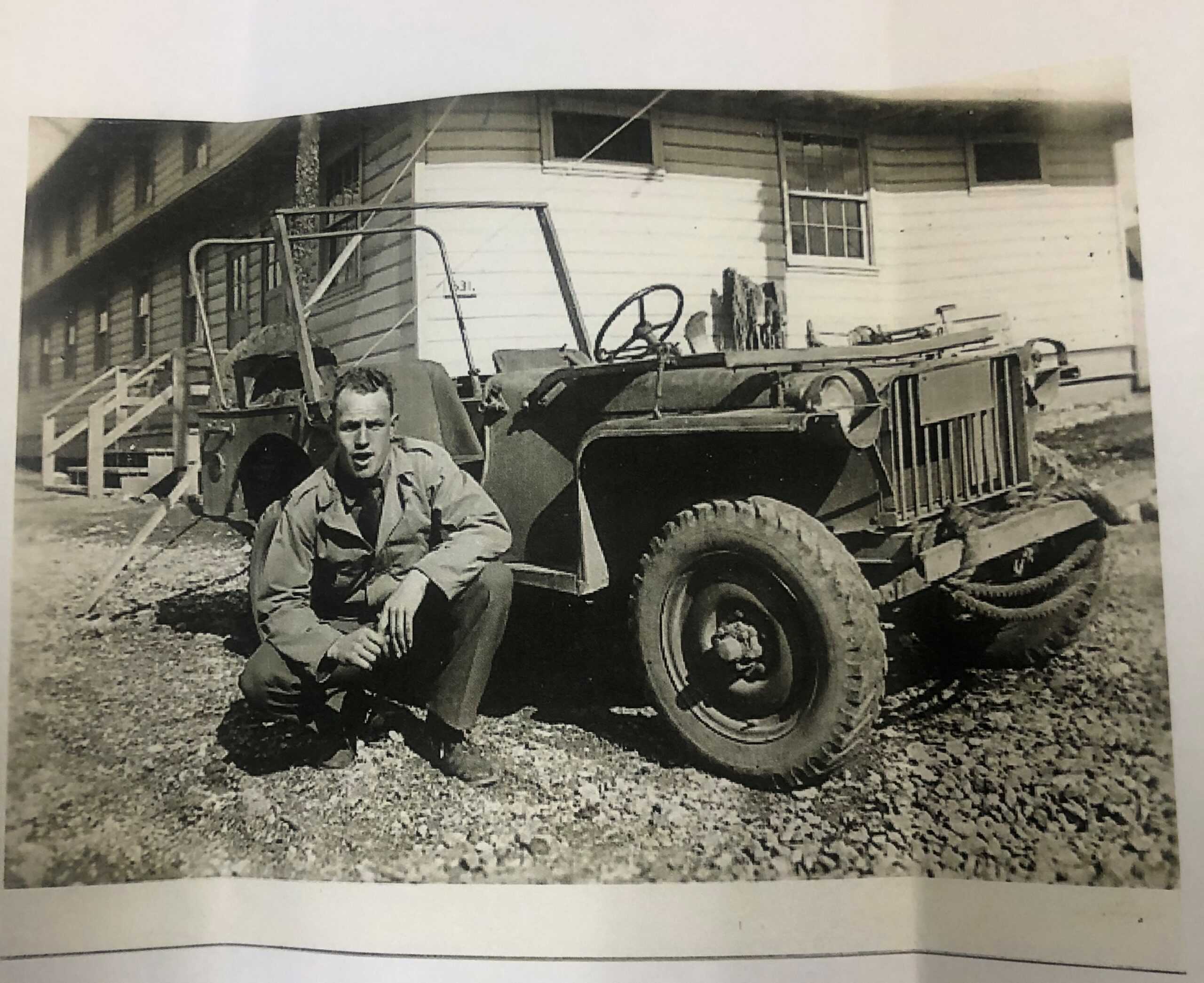 James Renard seated beside a military jeep outside a building.