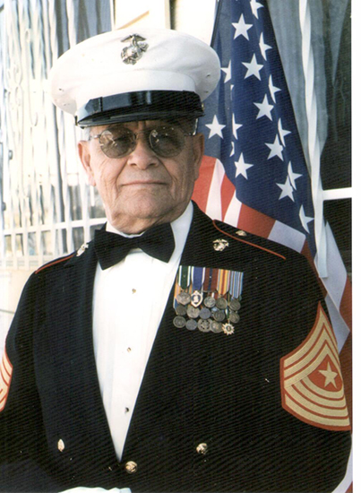 Veteran Jesse Louis Pacheco wearing a decorated uniform and cap in front of an American flag.