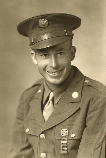 A person in a military uniform and cap, smiling at the camera. They are wearing a tie around their neck.