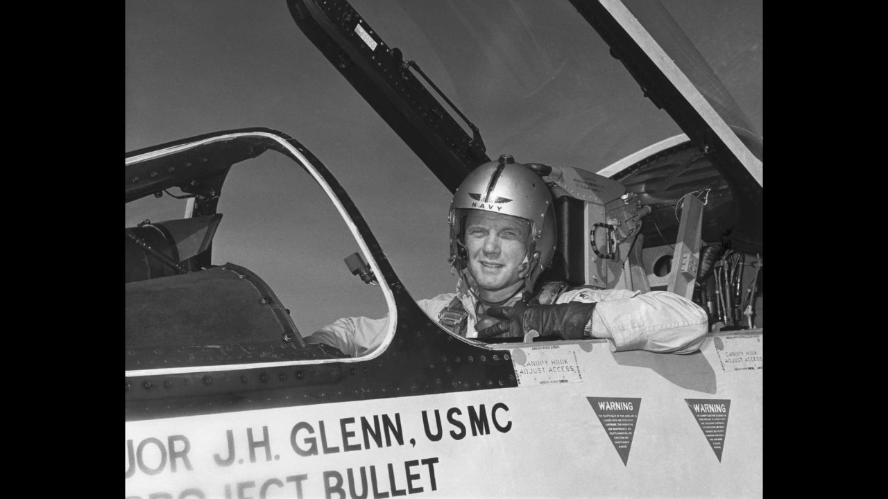 John Glenn seated in an aircraft cockpit wearing a flight helmet.