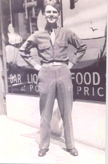 John Francis Kloecker standing in uniform before a wartime food sign.