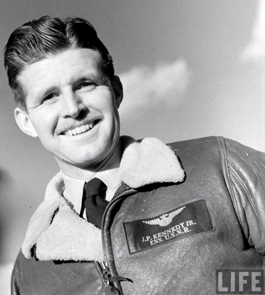 Smiling young man shown in a formal black-and-white portrait.
