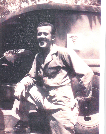 Smiling man seated indoors in a military uniform.
