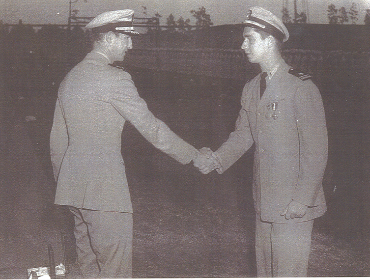 Two uniformed servicemen shaking hands outdoors.
