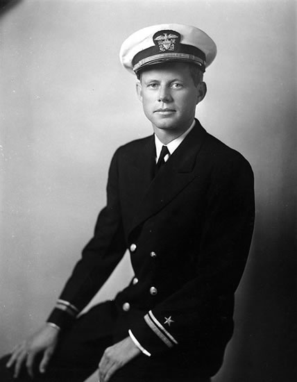 John Kennedy wearing a dark military dress uniform and peaked cap.