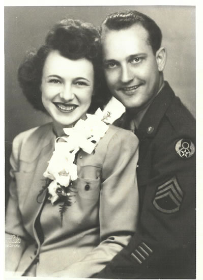 Couple posing for a portrait; man in military uniform next to a woman in a dress with a corsage.