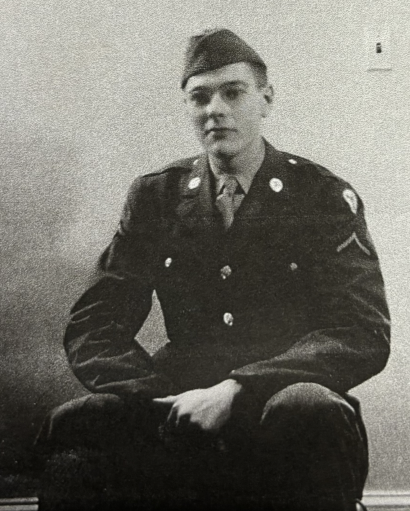 Young serviceman seated indoors in a military uniform.