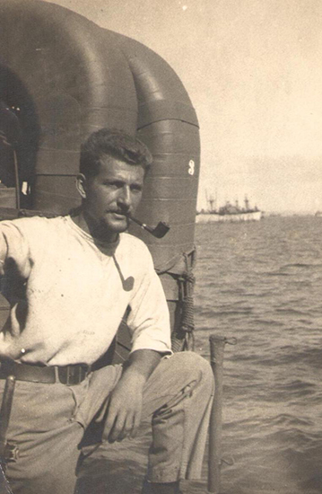 Lorence Resnick seated beside a military vehicle with a pipe in his mouth.