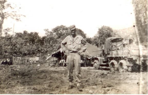 Serviceman standing near military tents and equipment outdoors.