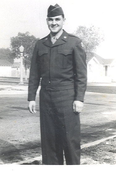 Serviceman posing outdoors in a dark military uniform.