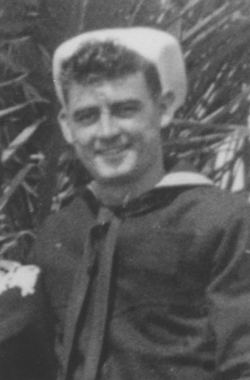 Smiling sailor wearing a dark naval uniform outdoors.