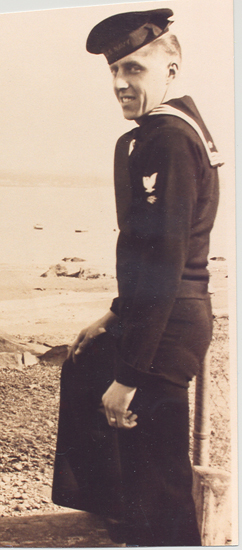 Serviceman standing outdoors in a dark military uniform.