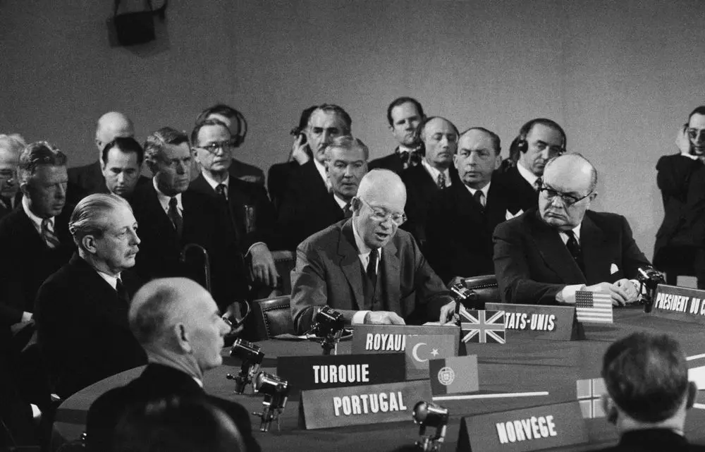 Historical black-and-white scene of international delegates seated at a NATO meeting.