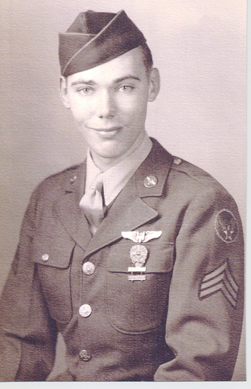 A black-and-white photo of a young man in military uniform, including an army cap and ribbons on his chest, posing for a portrait. He has short hair and is looking directly at the camera with a slight smile.