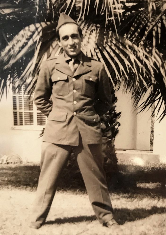 Serviceman standing outdoors beneath palm trees in military uniform.