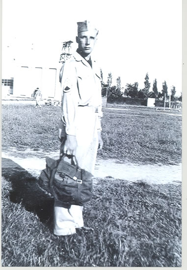 A man in military uniform standing while holding his luggage.
