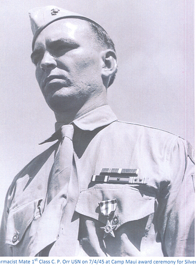 A black-and-white photograph of a man in military attire with a uniform and badges. He appears to be in an outdoor setting, with sunlight casting shadows. The man is wearing a hat and looking slightly off to the side.