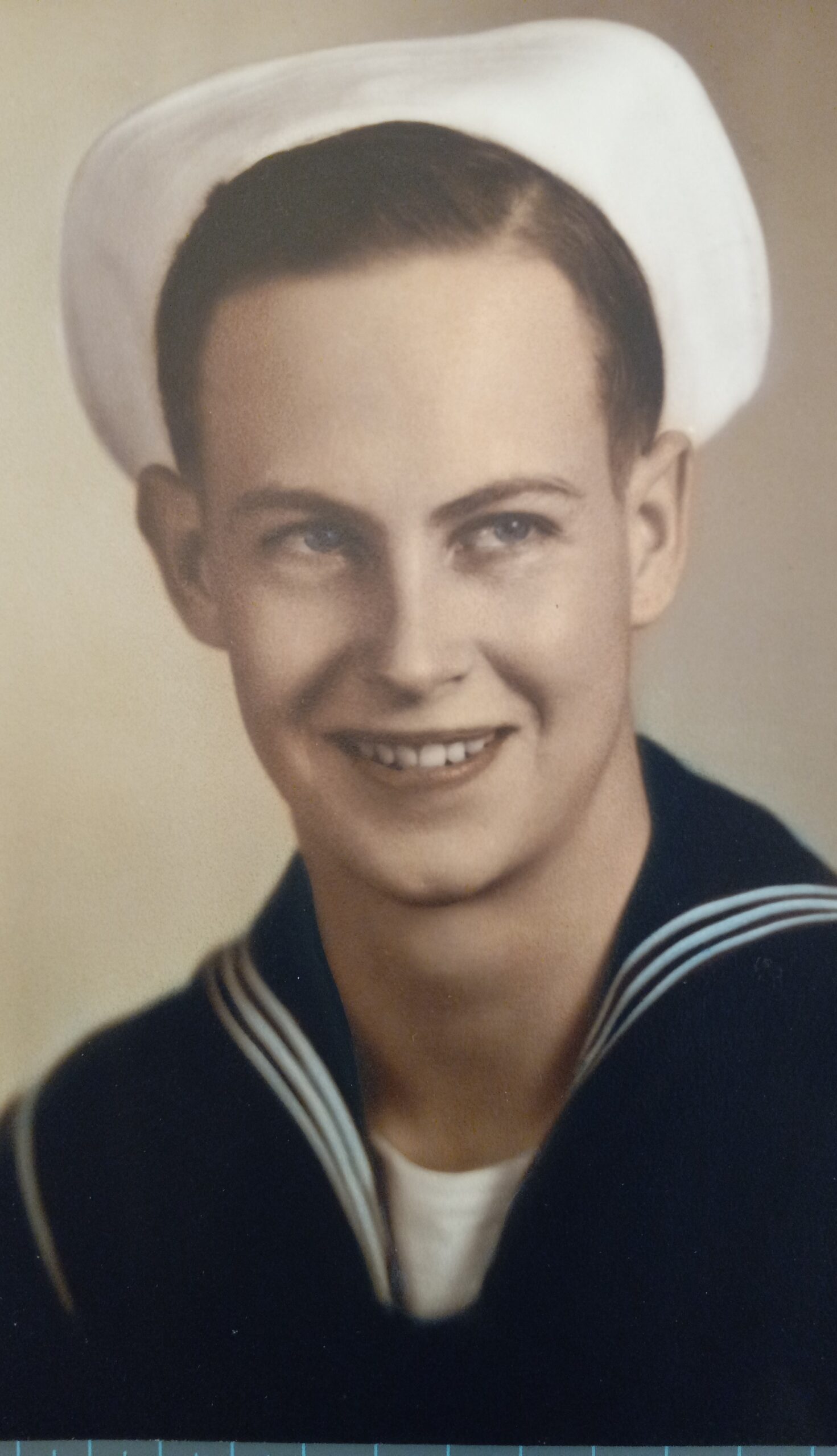 Smiling sailor wearing a white naval cap.