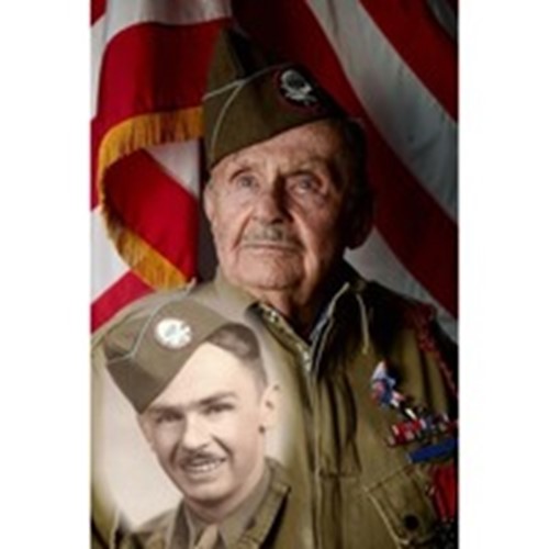The photograph is of an older man in military uniform wearing a tie and medals. He is standing in front of a flag.