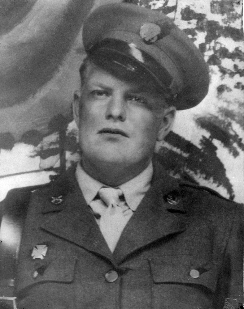 Serviceman wearing a military uniform and peaked cap outdoors.