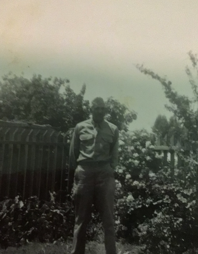 Serviceman standing outdoors near trees in a military uniform.
