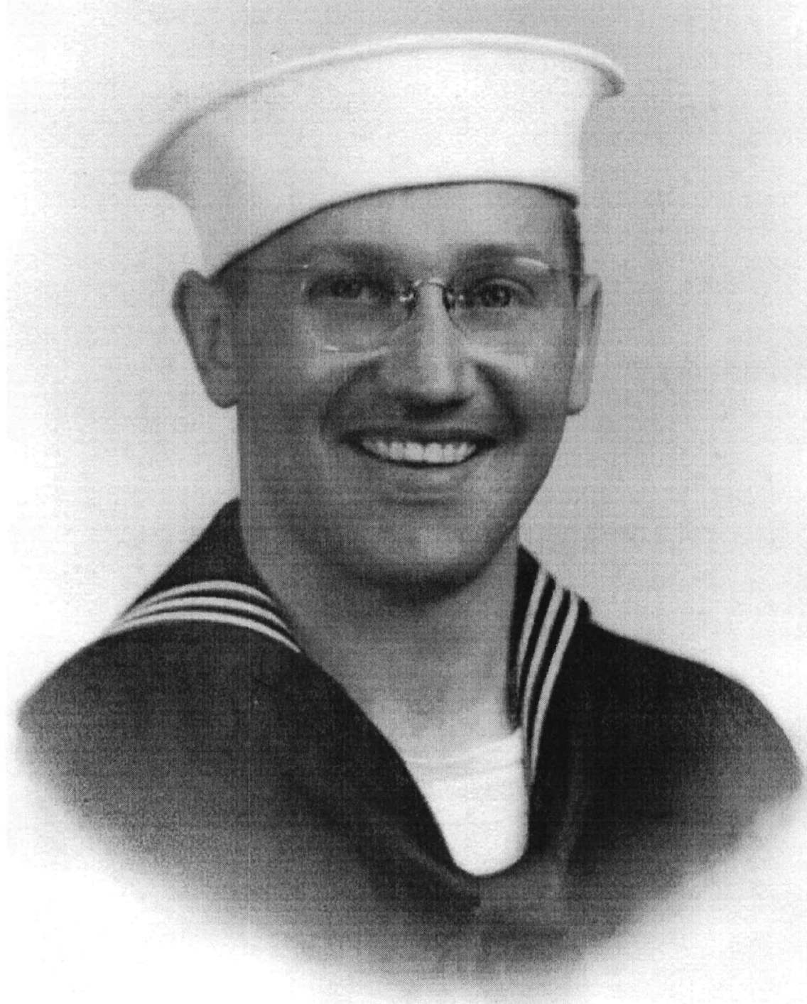 Smiling sailor wearing a white U.S. Navy cap and glasses.