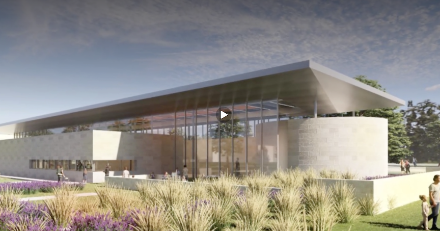 Video still showing a modern glass-walled building with a covered entrance and native landscaping.