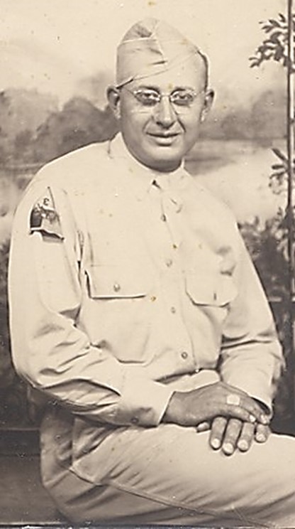 Serviceman wearing a light-colored military uniform in a formal portrait with a nature background.