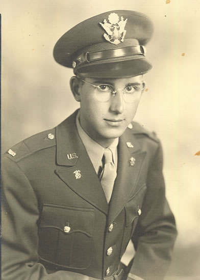 Serviceman wearing glasses, a U.S. Army uniform, and a peaked cap.