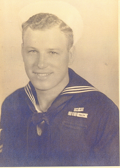 This is an old black and white photo featuring a man in a military uniform. He is smiling and wearing a tie with a sailor's collar insignia.