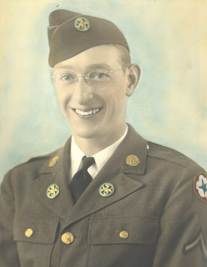 A sepia-toned photograph featuring an individual in military attire, wearing a cap with an emblem on the front and glasses, smiling directly at the camera.