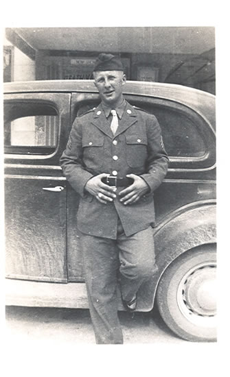 Serviceman standing beside a vintage car in military uniform.