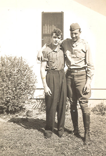 Two servicemen standing together outdoors in military uniforms.