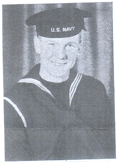 A U.S. Navy sailor in uniform posing for a photo. He is smiling at the camera.