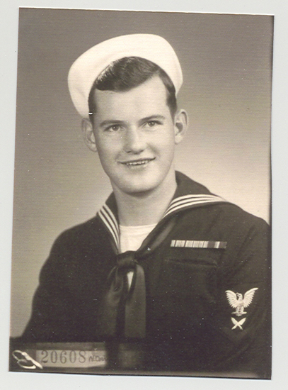 A sailor in uniform, posing for portrait. He is smiling and looking at the camera.