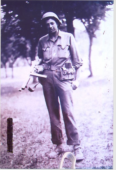 Serviceman standing outdoors in military gear with equipment at his waist.