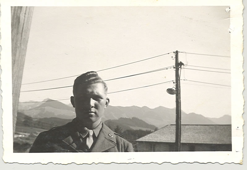 Young serviceman standing outdoors with mountains behind him.